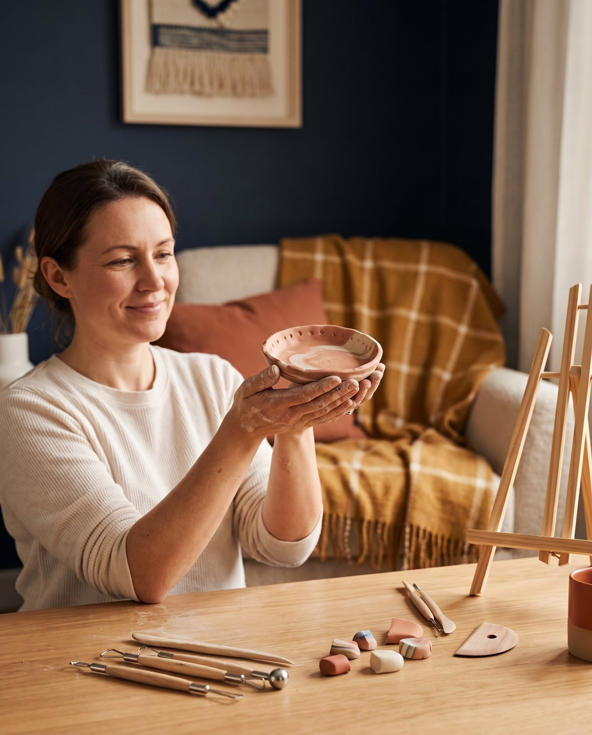 Een vrouw houdt trots een zelf geboetseerd schaaltje van FIMO-klei vast, met boetseergereedschap op tafel
